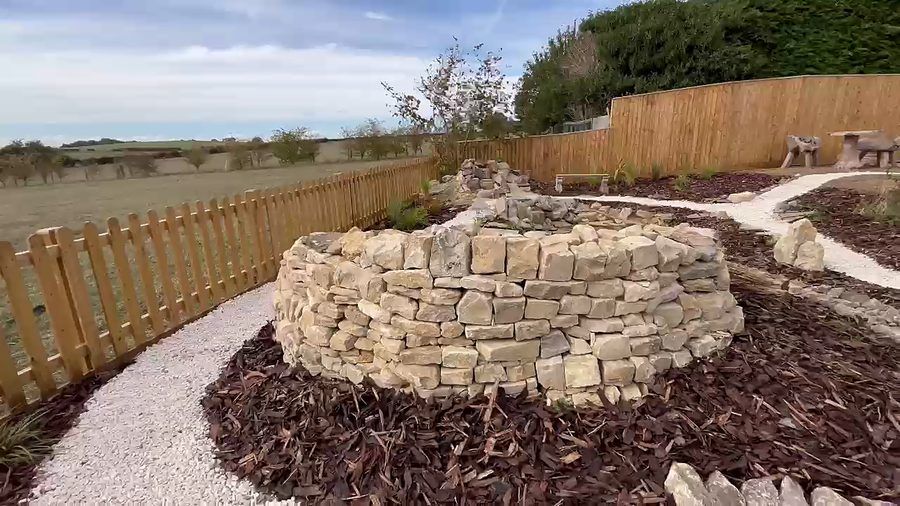 A circular drystone wall rising from a bed of bark mulch, ringed by a pale gravel path